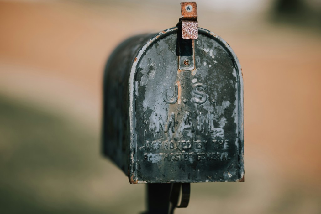 Old mailbox in front of distressed property being mailed as part of a campaign by a real estate investor.